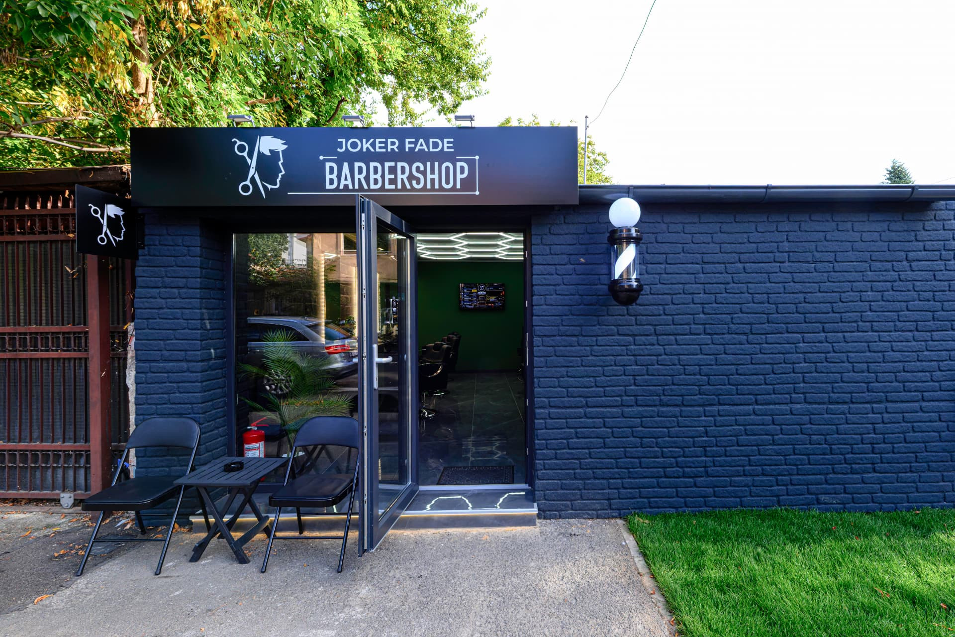 Intrarea Joker Fade Barbershop cu ușa deschisă și terasă cu scaune