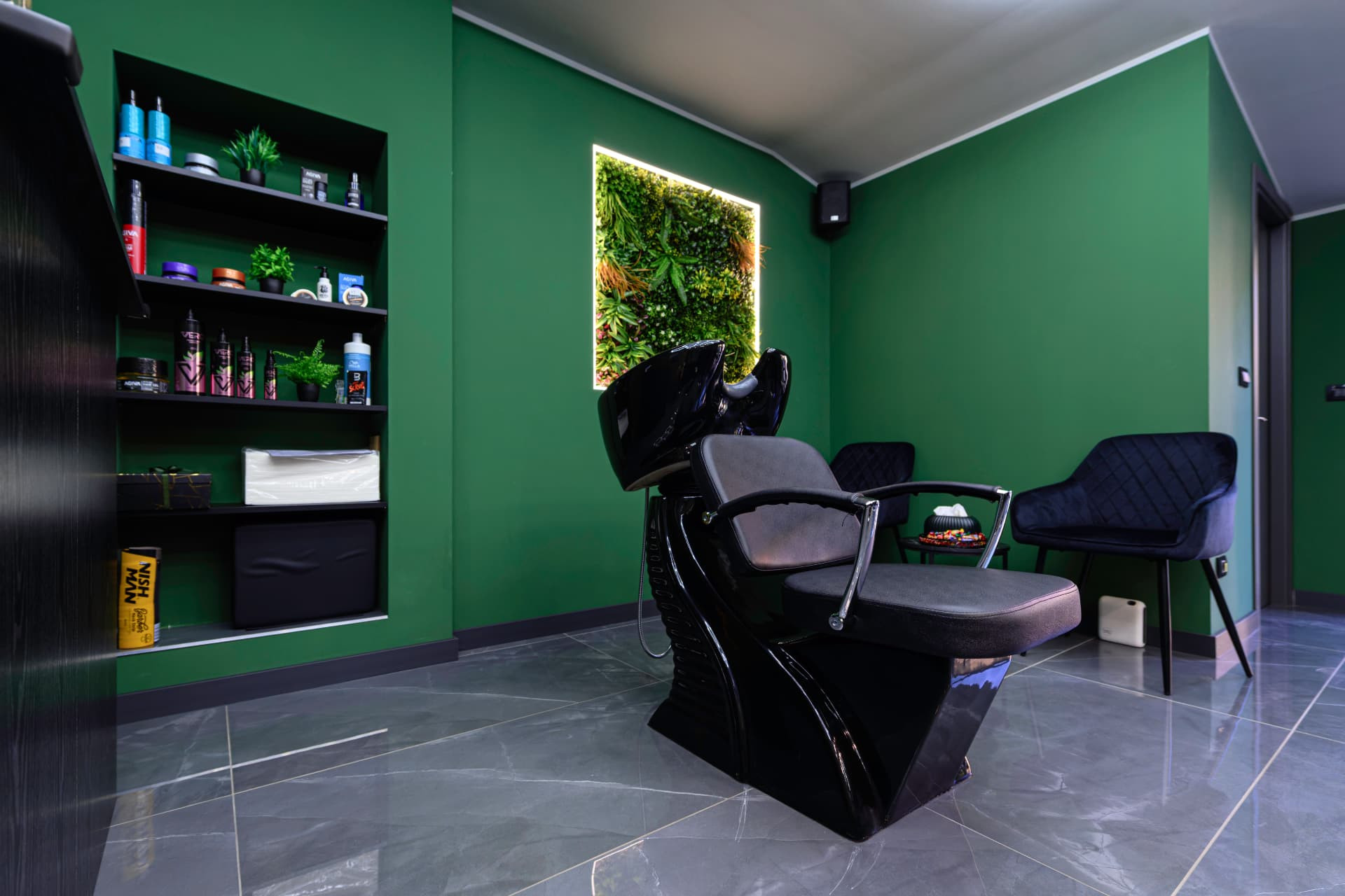 Chiuvetă neagră, raft cu produse și fotolii de așteptare în Joker Fade Barbershop